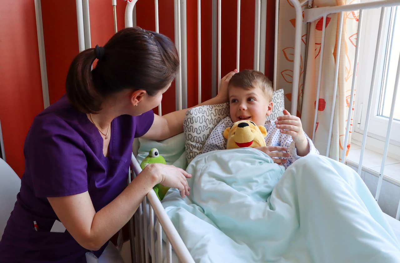 Nővér beszélget egy kisfiúval a kórházi ágy mellett