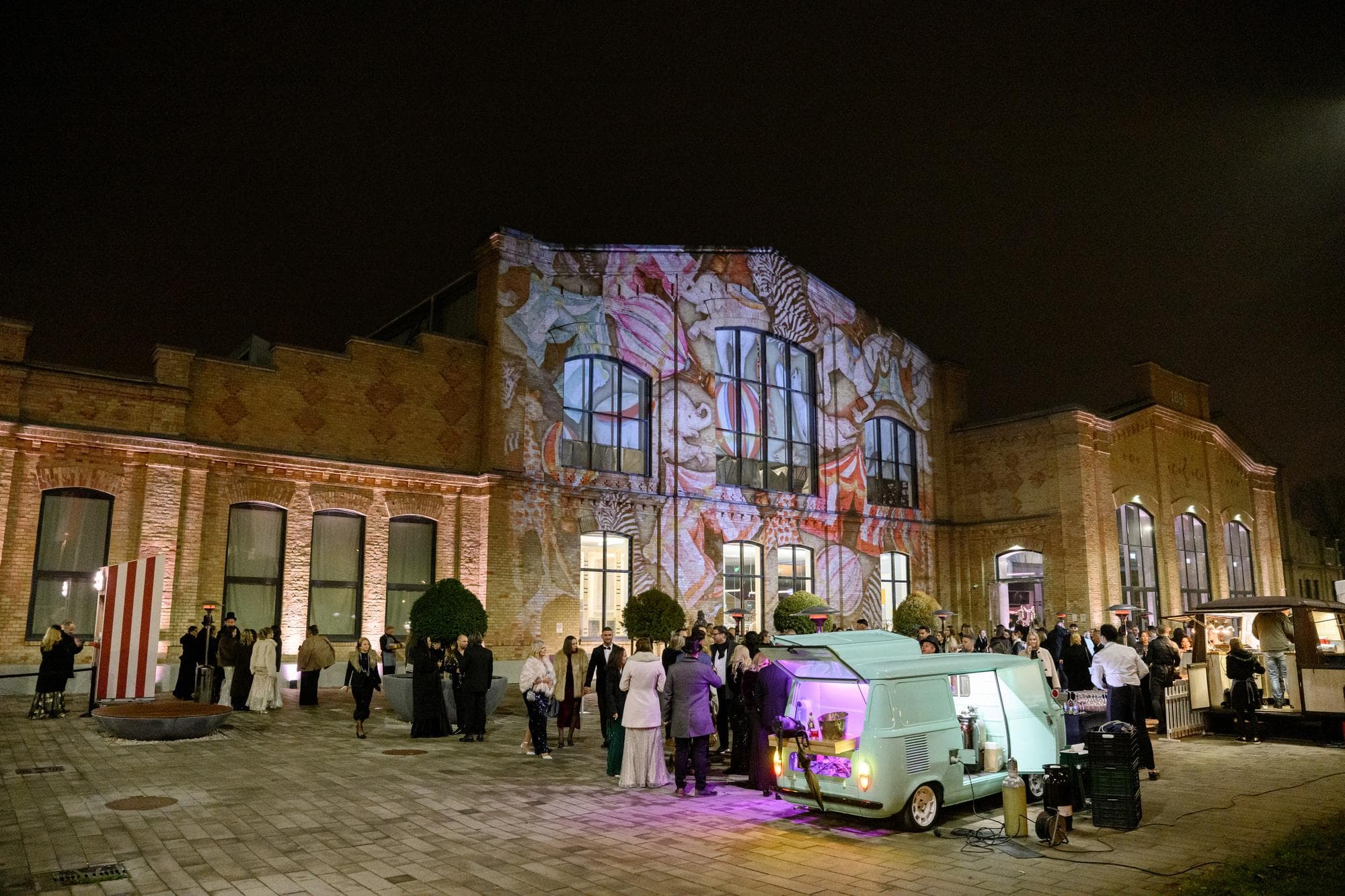 Vendégek a Hungarian Wedding Gala estéjén, színes fényfestéssel megvilágított épület előtt